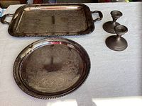 Photo showing 2 silver-plated serving platter trays by William Rogers and 2 sterling silver candlestick holders on a white patterned cloth surface