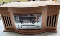 Front view showing wooden casing, brand logo, and silver radio/CD control panel with buttons and knobs