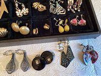 Tray with various vintage clip earrings including gold-tone ribbed and smooth pieces, white drop and diamond-shaped floral enamel earrings