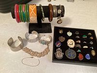 Overall collection of colorful bangles on stand, silver cuff bracelets, charm bracelet, and tray of rings and pendants