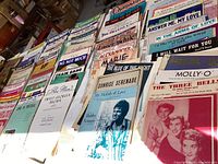 Top view showing multiple stacks of vintage sheet music spread out on a surface.