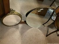 Photo showing two round mirrors, one small with decorative brass frame, one large plain without frame, placed on carpeted floor.
