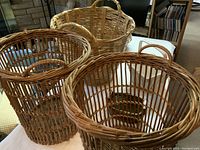 First photo showing a cluster of several wicker baskets, varying in shape from round to slightly oval, some with handles.
