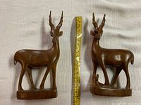 Two wooden antelope figurines shown side-by-side with tape measure indicating height approximately 7 inches.
