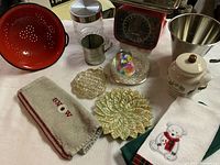 Overview of various vintage kitchen items including towels, scale, glass containers, colander, and candle drip holders on a white surface.