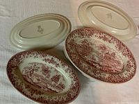 Top side of the oval dishes showing detailed red transferware scenic and floral patterns. Back stamps visible on the cream-colored ceramic base indicating 'Maddock Made in England'. Two dishes face down, revealing maker marks.
