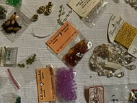 Various vintage beads, including faceted amber and purple beads, pearl-like strands, packaged gold metal beads and jewelry findings on cloth surface.