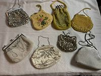 Front view of all 8 vintage evening bags laid out on fabric, showing variety of colors, materials, and chain/cord handles