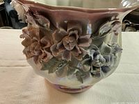 Side view showing detailed raised floral decoration with pink and purple flowers and green leaves on glazed ceramic flower pot.