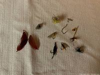 Various artificial fly fishing lures and hooks laid out on textured fabric, showing different sizes, colors and materials including feather, fur, and metal.