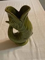 Angle view of green ceramic fish-shaped jug showing detailed fish head spout and curling body.