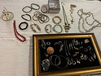 Full view of assorted jewelry including necklaces, bracelets, rings, earrings, and pendants arranged on a table and in a display frame.
