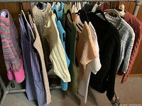 Collection of handmade sweaters and dress hanging on a rack, showing various colors and knit styles.