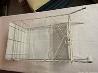 White painted vintage metal stand showing side profile, scrollwork, and wire grid shelf below.