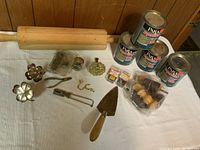 Lot contents overview showing 4 paint cans, multiple small tools and hardware items on a white cloth beneath wood panel wall