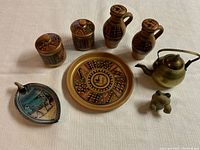 Front view of the pottery items, brass teapot, ceramic frog figurine, and decorative dishes arranged on white cloth.