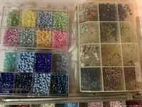 Top view of three clear plastic storage cases with many small compartments filled with colorful round and shaped beads