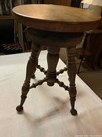 Full view of the antique wooden piano stool showing round seat and turned legs with metal feet, on a carpeted floor.