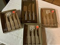 Four boxed sets of cutlery/cheese knives and silverware, showing brand names GS and Tramontina, items are new in original packaging.