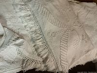 Close up of the white woven vintage bedspread showing textured diamond pattern and fringed border.
