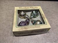 Original box labeled 'Christmas Classics' containing four hand-decorated glass ornaments visible through clear window.