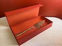 Metal Christmas tree shaped cake server inside open red box displaying the item.