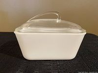 Side view of white rectangular opaque baking dish with clear glass lid on top showing profile and handle of lid.