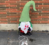 Full view of the elf decoration showing its size and shape in front of a brick wall.