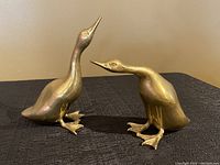 Pair of brass duck sculptures, one with neck upright, the other bent forward.