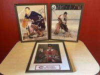 Three framed hockey prints placed on a table against a red wall: two action shots of goalies wearing Toronto Maple Leafs and Philadelphia Flyers jerseys, and one portrait of a Montreal Canadiens player.