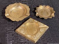 Top view of three vintage brass ashtrays showing their distinct shapes and detailed engravings