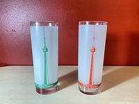 Two Dominion CN Tower drink glasses with CN Tower graphic and colored stripes on a reddish background.
