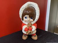 Front view of vintage ceramic figurine of girl in red parka holding a small brown puppy.