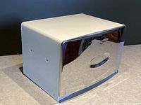 Closed view of vintage bread box showing white enamel sides and chrome front door with handle and latch