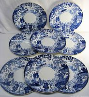 Eight Royal Crown Derby Mikado dinner plates arranged in display, showing blue and white Asian-inspired pattern with gold edges.
