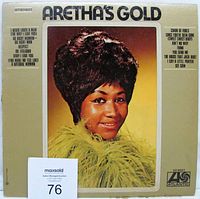 Front cover of Aretha Franklin's 'Aretha's Gold' vinyl LP with beige background, photo of Aretha in feathered garment, and track listing on sides.
