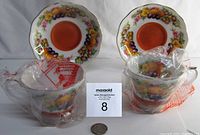 Two Royal Albert Country Fayre Dorset teacups and saucers in original bags beside a quarter for scale.