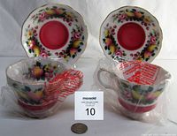 Two teacups and two matching saucers displayed with original plastic protective bags and a coin for scale.