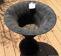 View down into top of cast iron planter showing flared rim and drainage hole inside bottom. Some dirt and surface wear visible.