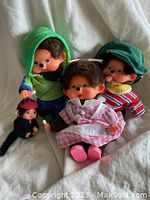 Photo showing four MonChhichi dolls seated on a fabric surface, featuring different outfits and sizes