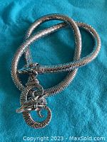 Photo of the full snake skin style necklace coiled on a blue fabric background, showing the overall texture and design.