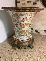 Side view showing the hand-painted floral porcelain body with gold rim and bronze decorative base.