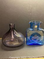 Two Blenko glass vases side by side, purple rounded vase and blue square vase