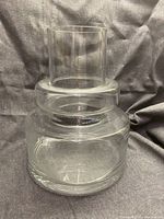 Front view of the large clear glass vase on a dark fabric background, showing cylindrical base and neck.