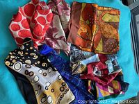 Overview of nine mixed silk scarves arranged and folded on a blue cloth background.