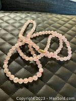 Full view of the rose quartz beaded necklace laid on a black quilted surface showing its length and bead details.