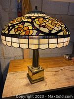 Full view of Tiffany style lamp showing stained glass shade with floral pattern and brass base on wooden surface.