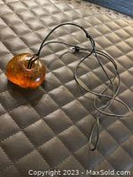 Photo showing the amber pendant attached to the leather string necklace laid flat on a quilted surface.