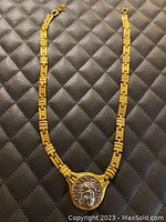 Full view of necklace showing rectangular patterned chain and central medallion with Roman face design.