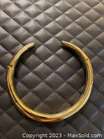 Wide, polished gold-tone choker necklace with a smooth finish placed on a quilted black surface. The necklace is circular with open ends showing a hinge mechanism on each side.